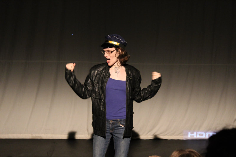 An artist in a leather jacket holds their arms up with biceps flexed