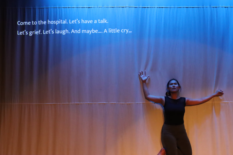 A dancer on her with her arms spread wide up against a screen with a variety of text across the top. 